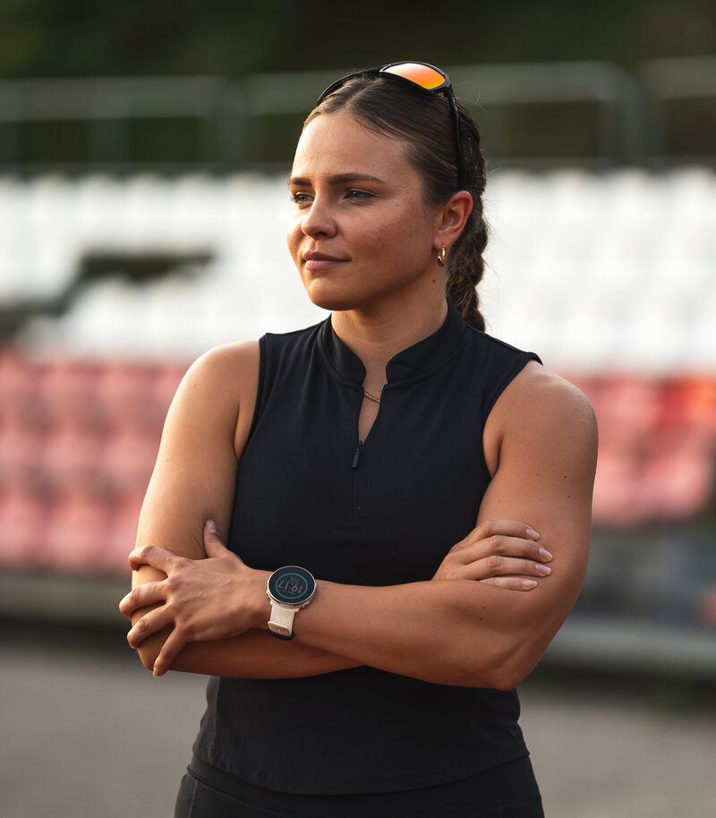 Portret trenerki personalnej Julii Kudlińskiej z założonymi rękami na tle trybun stadionu.