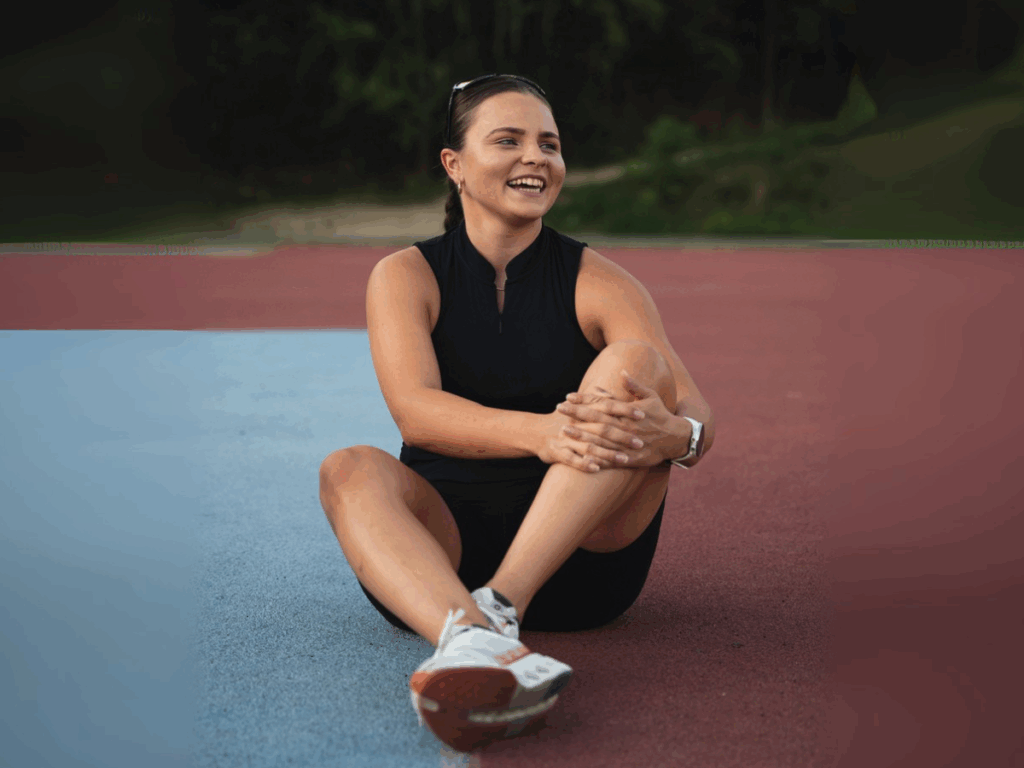 Uśmiechnięta trenerka personalna Julia Kudlińska siedząca na bieżni po zakończonym treningu.